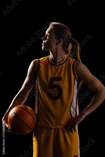 Young Caucasian female basketball player poses confidently in a basketball uniform on a black backgr