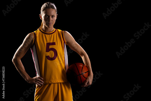 Confident young Caucasian female basketball player poses in basketball attire, with copy space on bl
