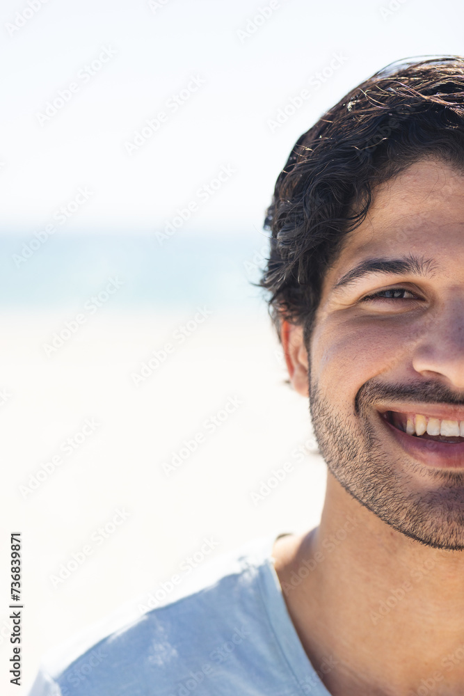Fototapeta premium Young biracial man smiles brightly outdoors at the beach, with copy space