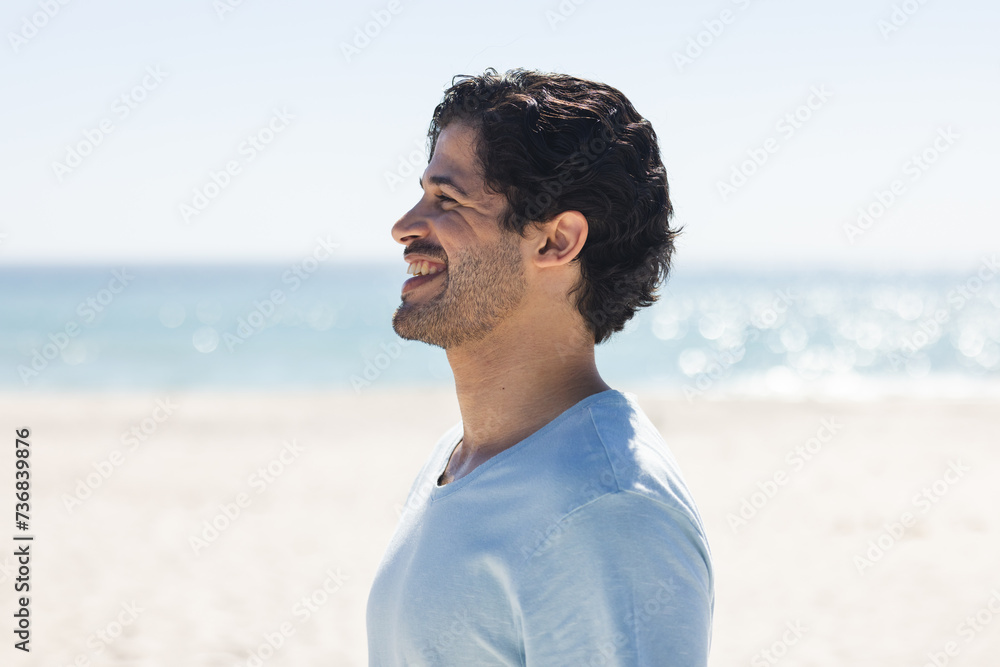 Fototapeta premium A young biracial man smiles brightly outdoors at the beach