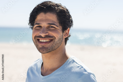 Young biracial man smiles brightly outdoors at the beach