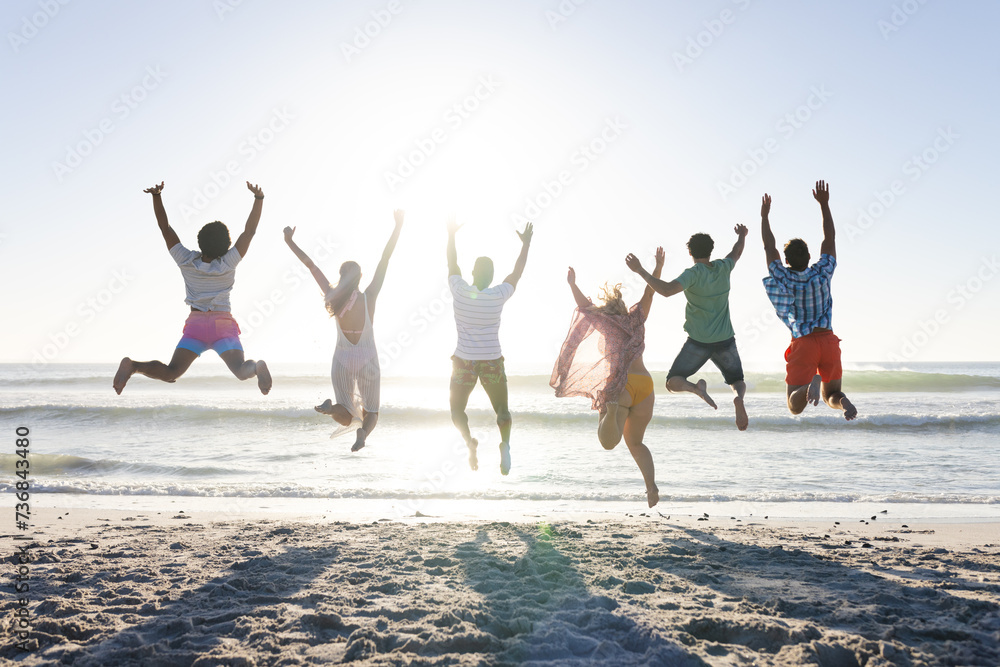 Fototapeta premium Diverse group of friends jumping joyfully on a sunny beach