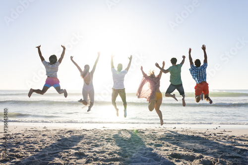 Diverse group of friends jumping joyfully on a sunny beach