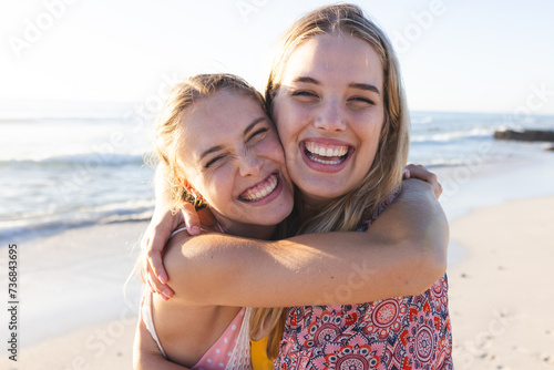 Caucasian young female friends embracing on a sunny beach