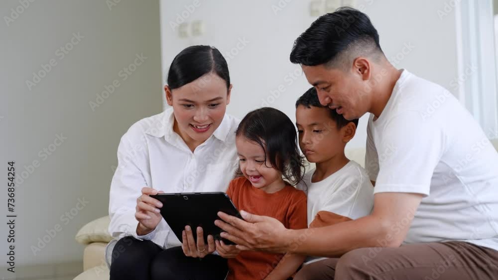 Happy Asian family using tablet, laptop for playing game watching movies, relaxing at home Happy Asian family using tablet, laptop for playing game watching movies, relaxing at home