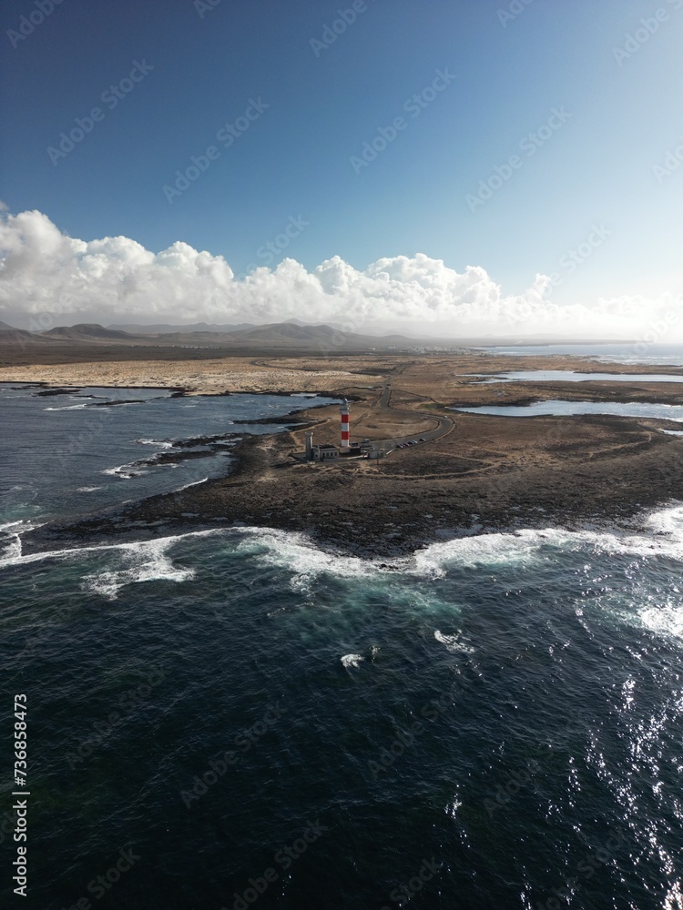 The 19th century red and white bands Faro del Tostón lighthouse located on the northwest coast of Fuerteventura in the Canary Islands. A lighthouse against the background of the blue sky and the ocean