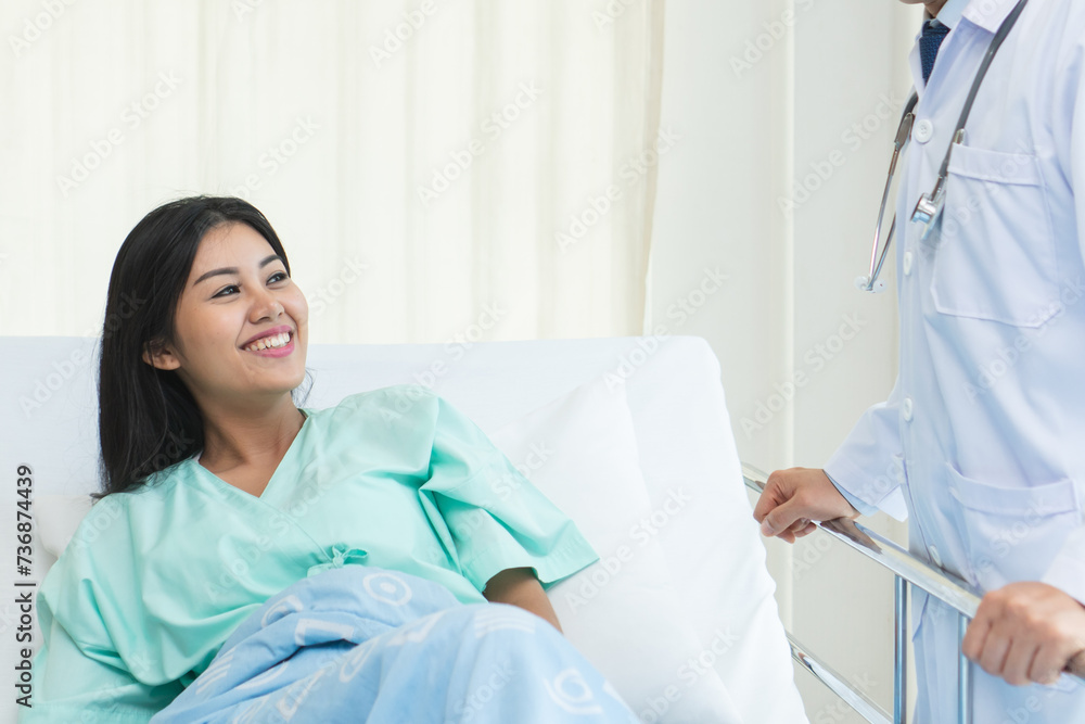 Obraz premium cheerful Asian doctor talking with young woman patient for monitoring and check up after surgery. doctor giving advice in the touchscreen to women to take care the lesion after out of hospital.