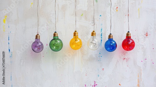 a group of multicolored light bulbs hanging from a string on a white painted wooden wall with paint splatters all around them.