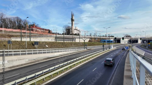 New city highway in Krakow, Poland, called Trasa Lagiewnicka. Tunnels for cars and trams and slip roads. Traffic, passing tram and railroad with passing train above. Church in the background. 4K video photo