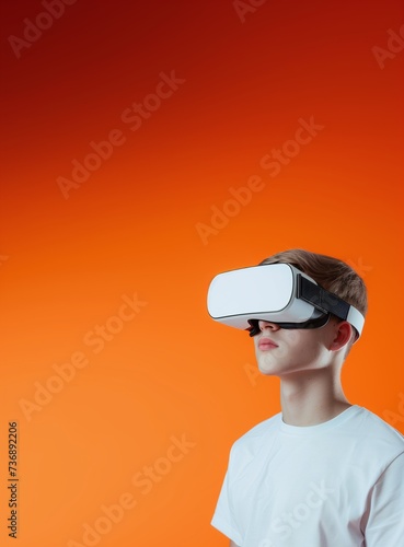 Western Blond Young Adult Man Wearing VR Headset, Enjoying Virtual Reality Experience on Gradient Orange Background. Isolated on the Right Side. Vertical Photo Portrait with Empty Copy Space © Clearmind