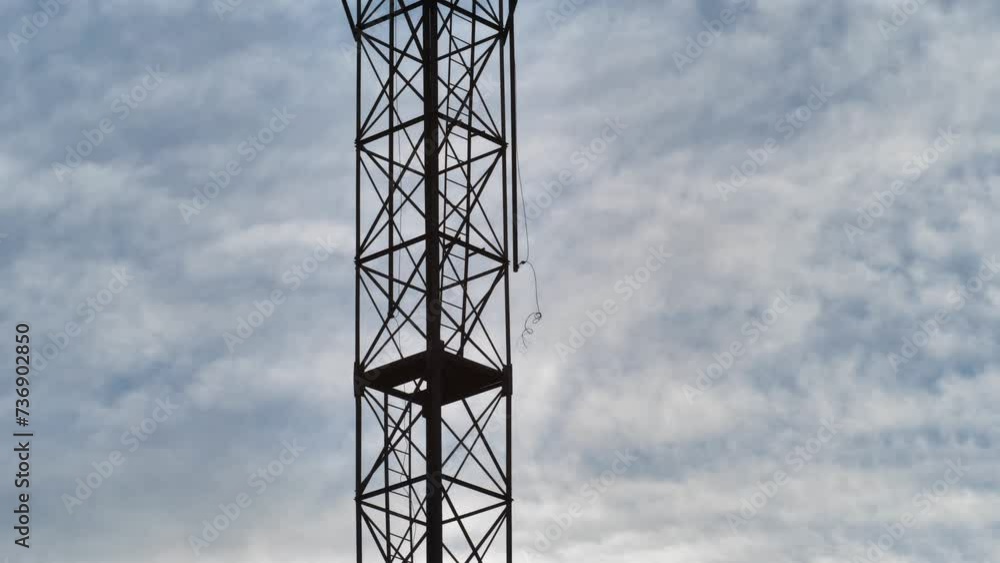 A tall metal observation tower with searchlights. Blue cloudy sky in the background. Old watchtower with broken wires. Architectural structure for a prison, military unit or storage area A tall metal observation tower with searchlights. Blue cloudy sky in the background. Old watchtower with broken wires. Architectural structure for a prison, military unit or storage area