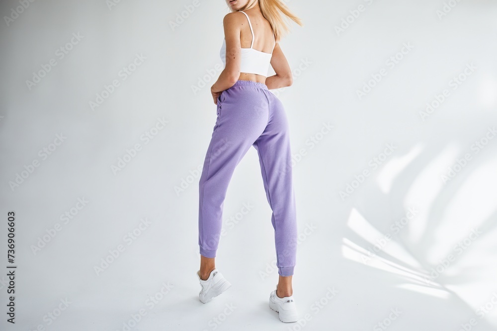 Athletic young girl wears a single color bright pants. Trousers for sports. Horizontal studio photo of A Fit young woman standing in modern joggers.