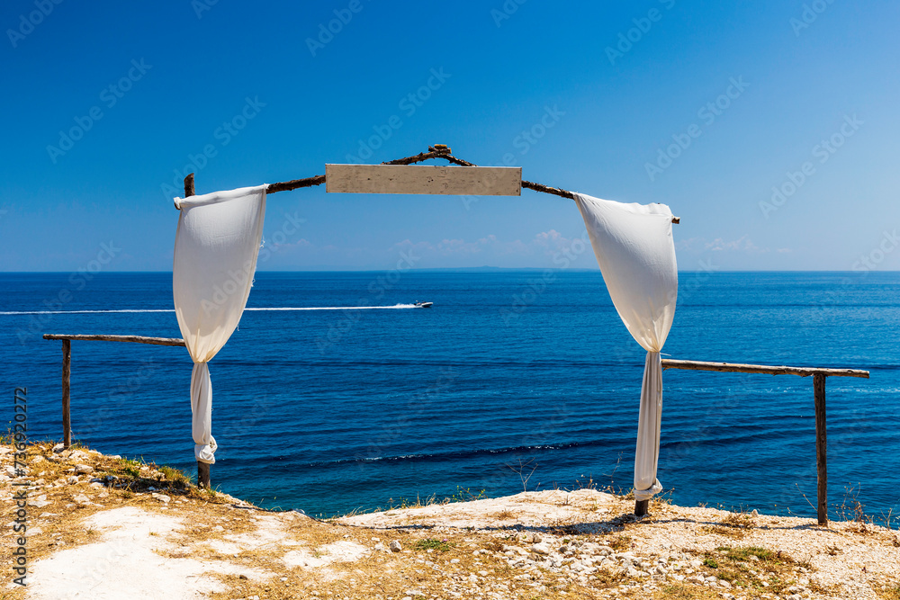 Empty wedding gate made of sticks and located on coastline of the sea, decorated by white fabric.