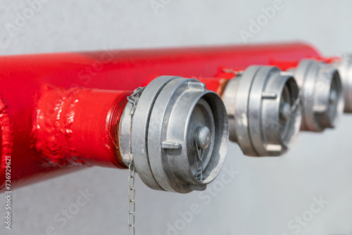 Red fire hose and water tap on white wall background