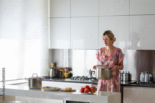Young housewife. Beautiful woman stands near table on kitchen at home. Housewife cooking on the kitchen in the morning.