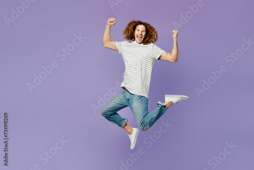 Full body young man wears grey striped t-shirt casual clothes jump high jump high doing winner gesture celebrate clenching fists say yes isolated on plain pastel purple background. Lifestyle concept.