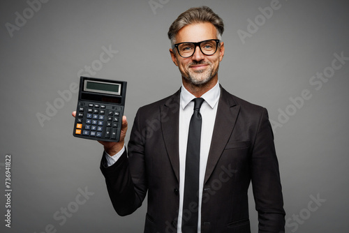 Adult successful employee business man corporate lawyer wear classic formal black suit shirt tie work in office use show calculator with blank screen isolated on plain grey background studio portrait.