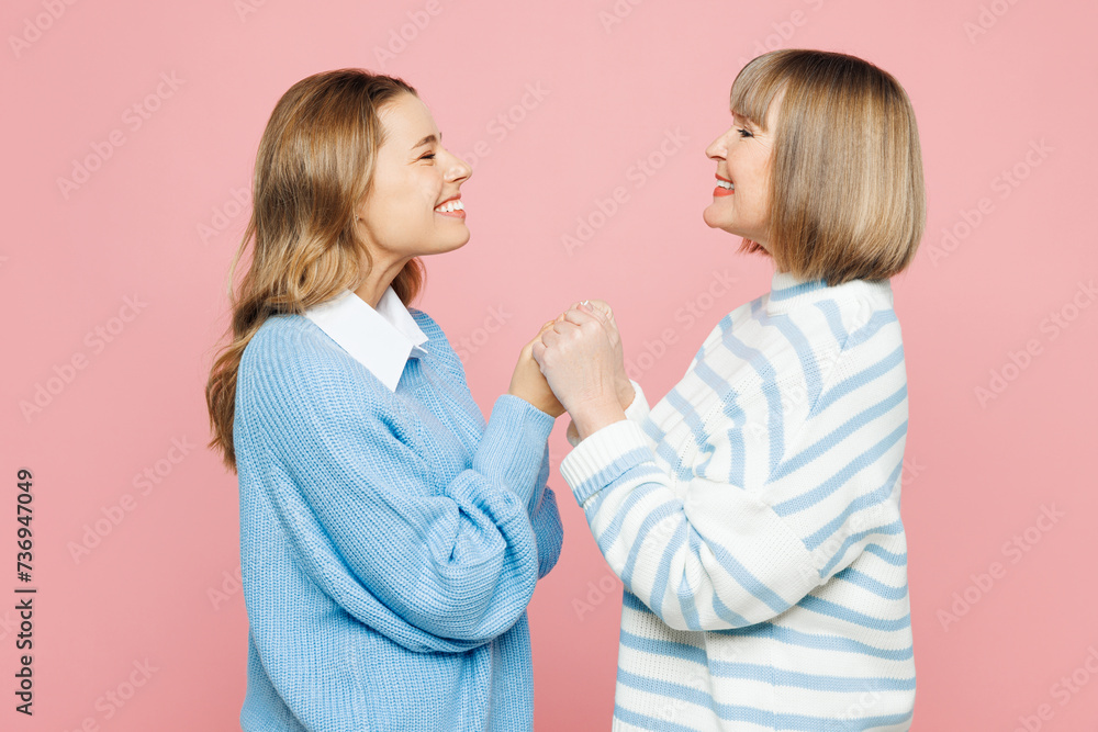 Side view elder parent mom 50s years old with young adult daughter two women together wear blue casual clothes hold hands look to each other isolated on plain light pink background Family day concept Side view elder parent mom 50s years old with young adult daughter two women together wear blue casual clothes hold hands look to each other isolated on plain light pink background Family day concept