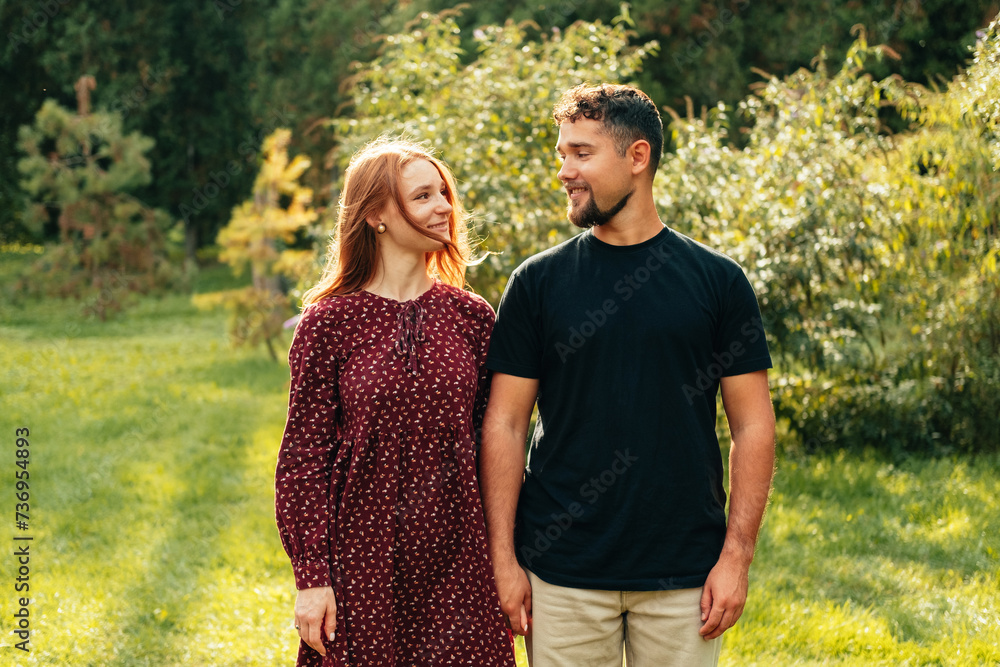 Fototapeta premium Outdoors shot of happy couple standing straight in park looking at each other on a sunny day.