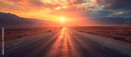 The afterglow of the red sky at sunset illuminates the desert road as the sun dips below the horizon, casting a warm glow over the natural landscape © 2rogan