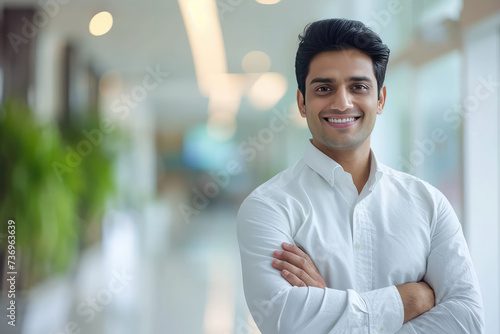 Handsome Indian male dentist smiling, standing with folded hands inside blurry modern clinic. Dental care concept © boxstock production