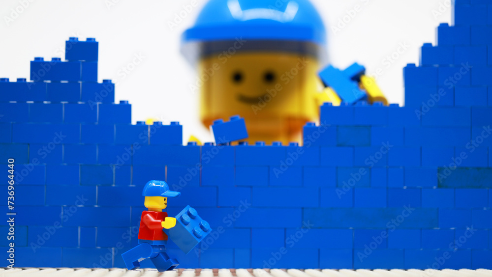 Obraz premium Hong Kong -February 15 2024: giant man build a brick wall piece by piece with his little helper 