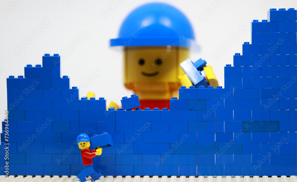 Naklejka premium Hong Kong -February 15 2024: giant man build a brick wall piece by piece with his little helper