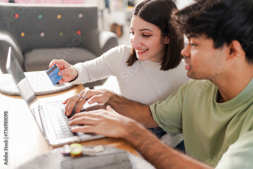 Happy couple engaged in an online purchase, with the man holding a credit card and the woman typing on a laptop photo