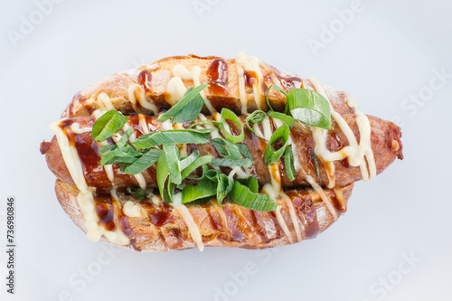 Close up top view of veal sausage hot dog in sweet potato bread with spring onions on white plate