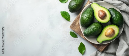 Top view of ripe avocados arranged on a white dish and wooden cutting board with cloth, creating a flat lay. Represents the concept of healthy fruits with space for text. photo