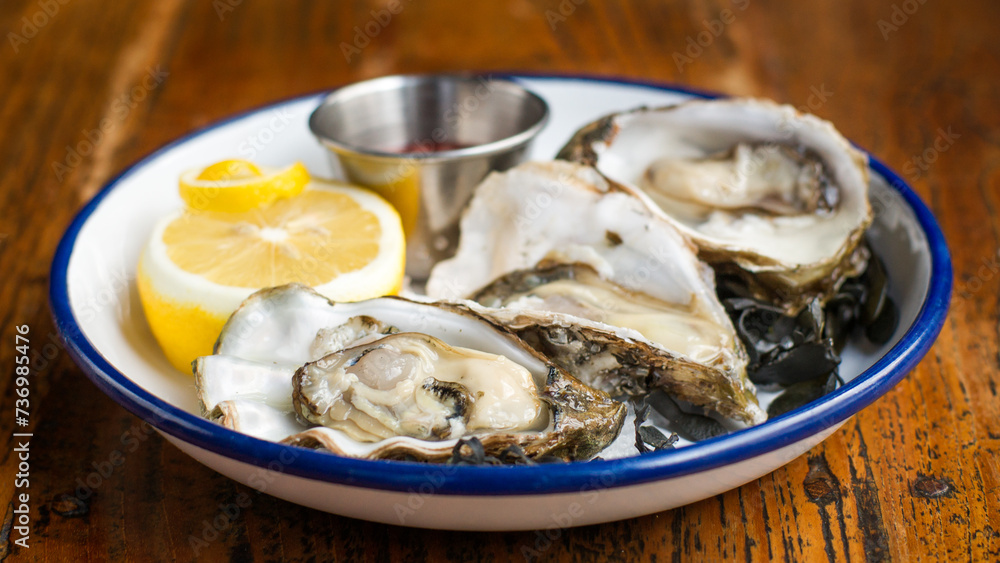 Three fresh oysters on a plate with lemon and mignonette on a wooden table in a restaurant Three fresh oysters on a plate with lemon and mignonette on a wooden table in a restaurant