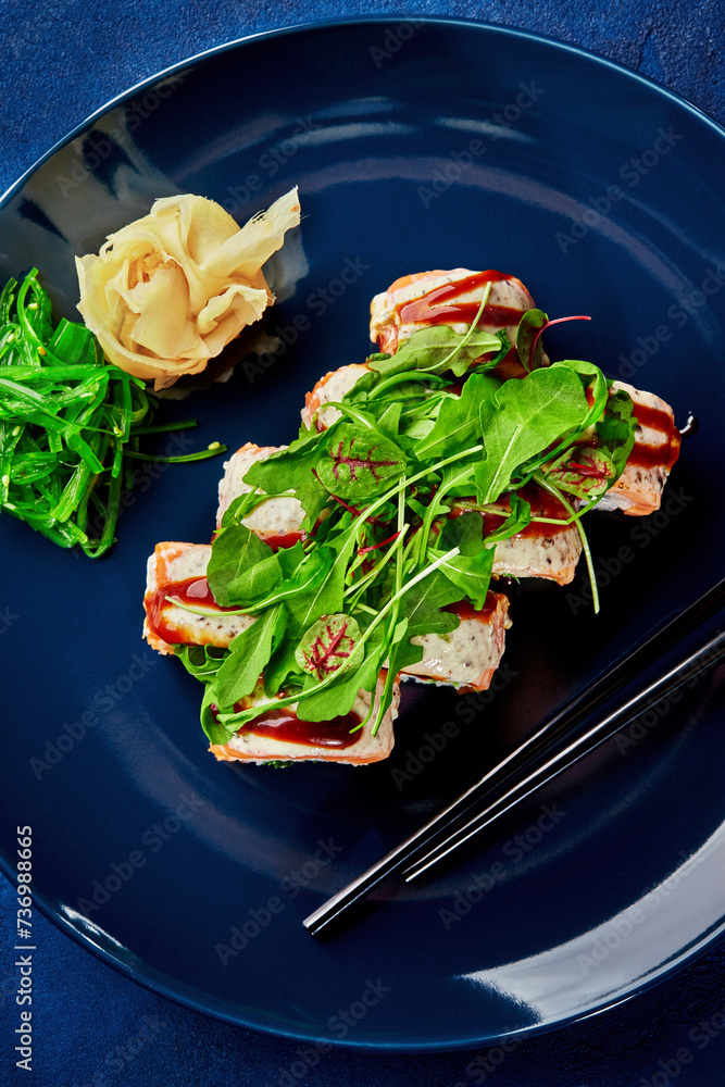 Gourmet sushi roll with salmon and greens on blue plate