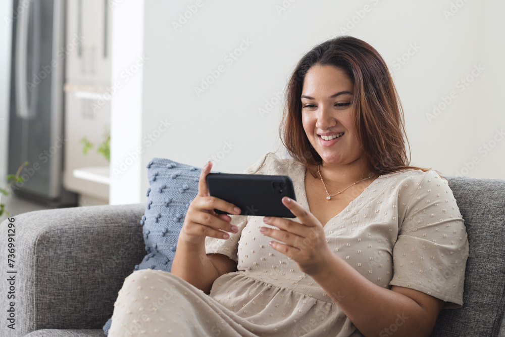 Young plus size biracial woman enjoys gaming on her phone at home, with copy space unaltered Young plus size biracial woman enjoys gaming on her phone at home, with copy space unaltered