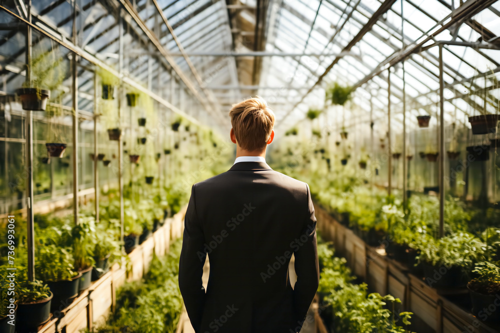 A man in a business suit stands with his back in a huge modern bright greenhouse - a vertical farm. Concept for the development of smart agriculture