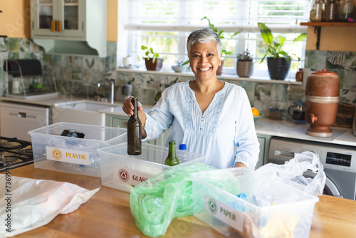 A mature biracial woman smilingly sorts recycling at home photo