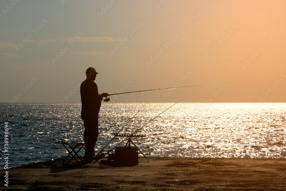A fisherman is fishing with afishing rod on the seashore, opposite the sun.
