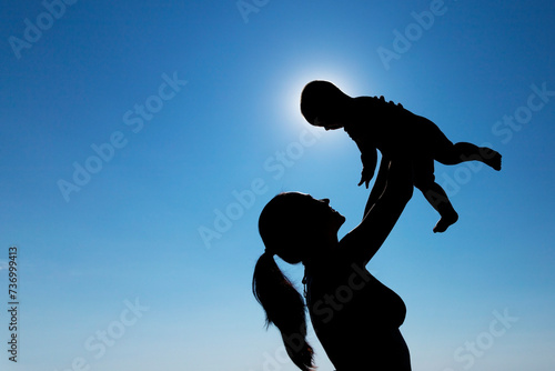 A young girl holds a child in her arms against the sun. Silhouette photography.