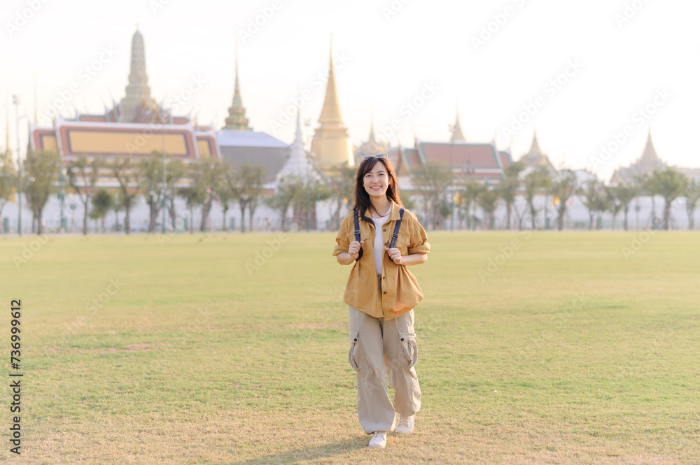 Fototapeta premium A Traveler Asian woman in her 30s exploring Wat Pra Kaew. From stunning architecture to friendly locals, she cherishes every moment, capturing it all in her heart and camera for years to come.