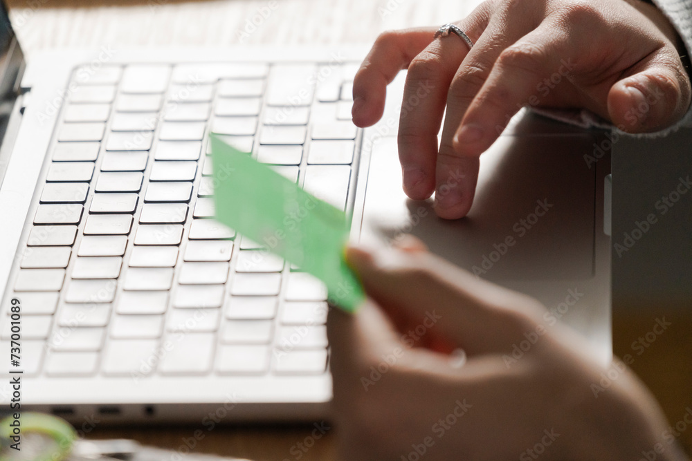 © Studio Marmellata - hand placing a credit card on a laptop trackpad, symbolizing a secure online transaction from home