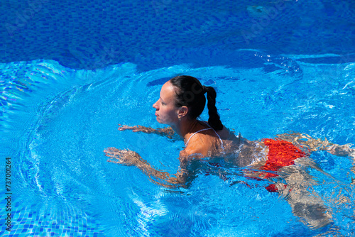 Top view of a tanned girl, female, model in a red swimsuit, swimming in the blue water of the pool.