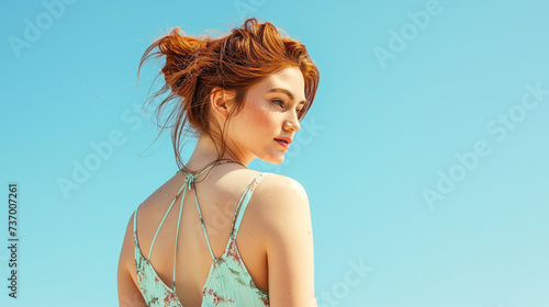 Redhead in an open-back sundress looking over shoulder, pastel sky-blue setting
