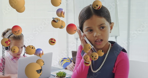 Image of digital interface with emoji icons floating over children using electronic devices