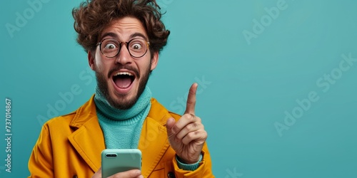 Happy young man holding a smartphone with a cheerful expression on his face, representing modern communication and success on a blue background. photo