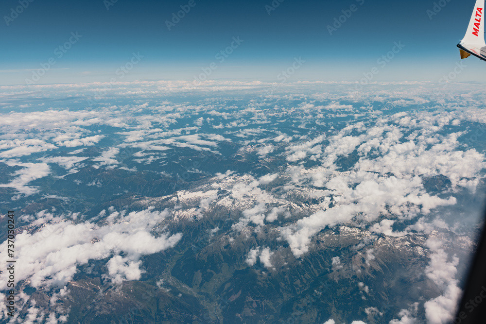 Milan, Italy - September 18, 2022. Aerial view of clouds and snowy mountains. Airplane view. Above the clouds