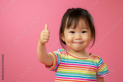 Happy little cute Asian girl giving thumbs up on pink background