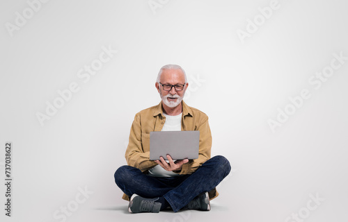 Full length of senior businessman working over laptop while sitting on isolated white background