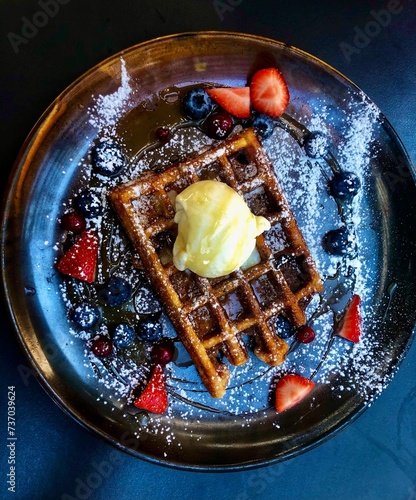Belgian waffle with ice cream, caramel, strawberries and bilberries in a black plate © Ligita