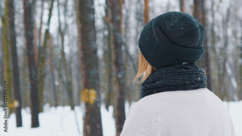 Back view of woman in winter clothes walking in the park snowy forest.