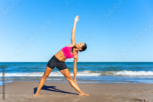 Middle aged woman exercising yoga on the beach this summer