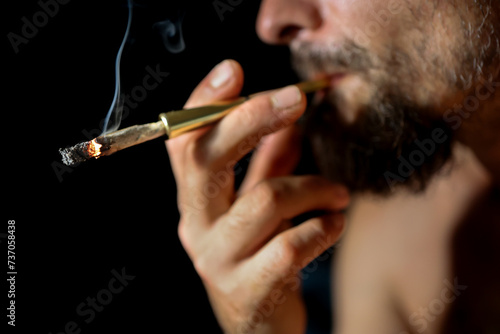 lit marijuana cigarette being smoked by a bearded man in close-up.